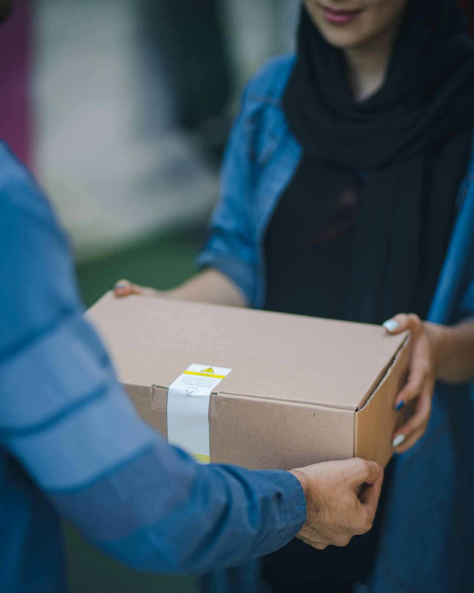 A courier handing a sealed cardboard parcel to a customer at their door