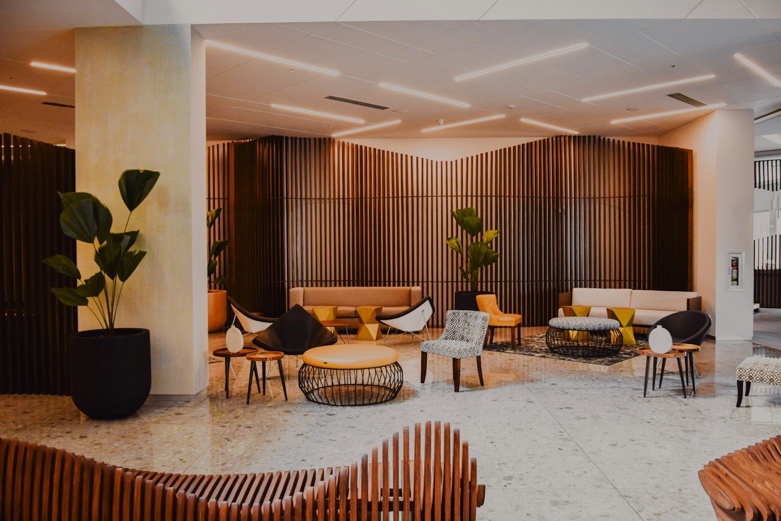 A hotel lobby lounge with armchairs, low tables and potted palms under warm lighting
